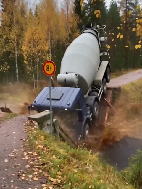 Sininen betoniauto on pudonnut keula edellä puroon romahtaneen puusillan kohdalla syksyisessä metsässä.